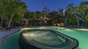A swimming pool with a curved edge, surrounded by trees and lounge chairs. - ANANA Yaaxlum 105 S (Tulum)
