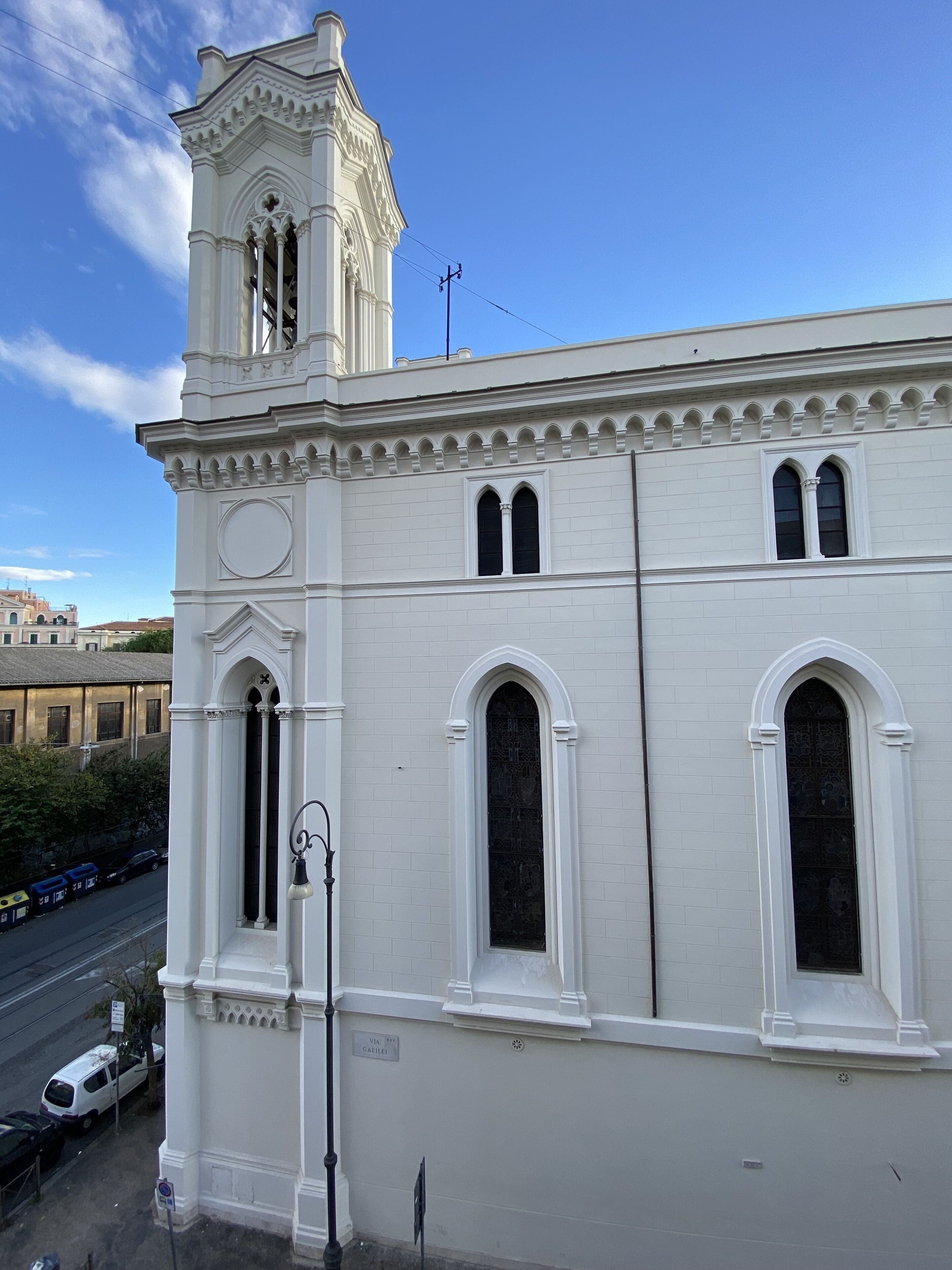 Um edifício branco com torre sineira, janelas em arco e vista para a rua.