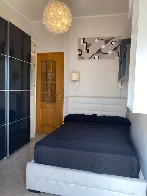 A bedroom with a bed, a wooden door, a wall-mounted lamp, and a decorative wall piece. - Domus romae esquilini (Roma)
