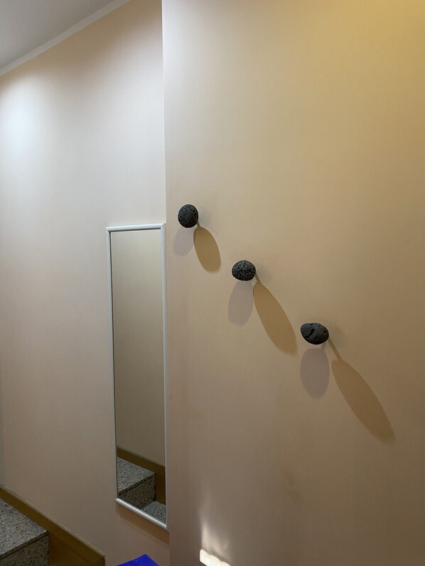Un couloir avec un miroir qui reflète un escalier et un mur orné de trois objets sphériques.