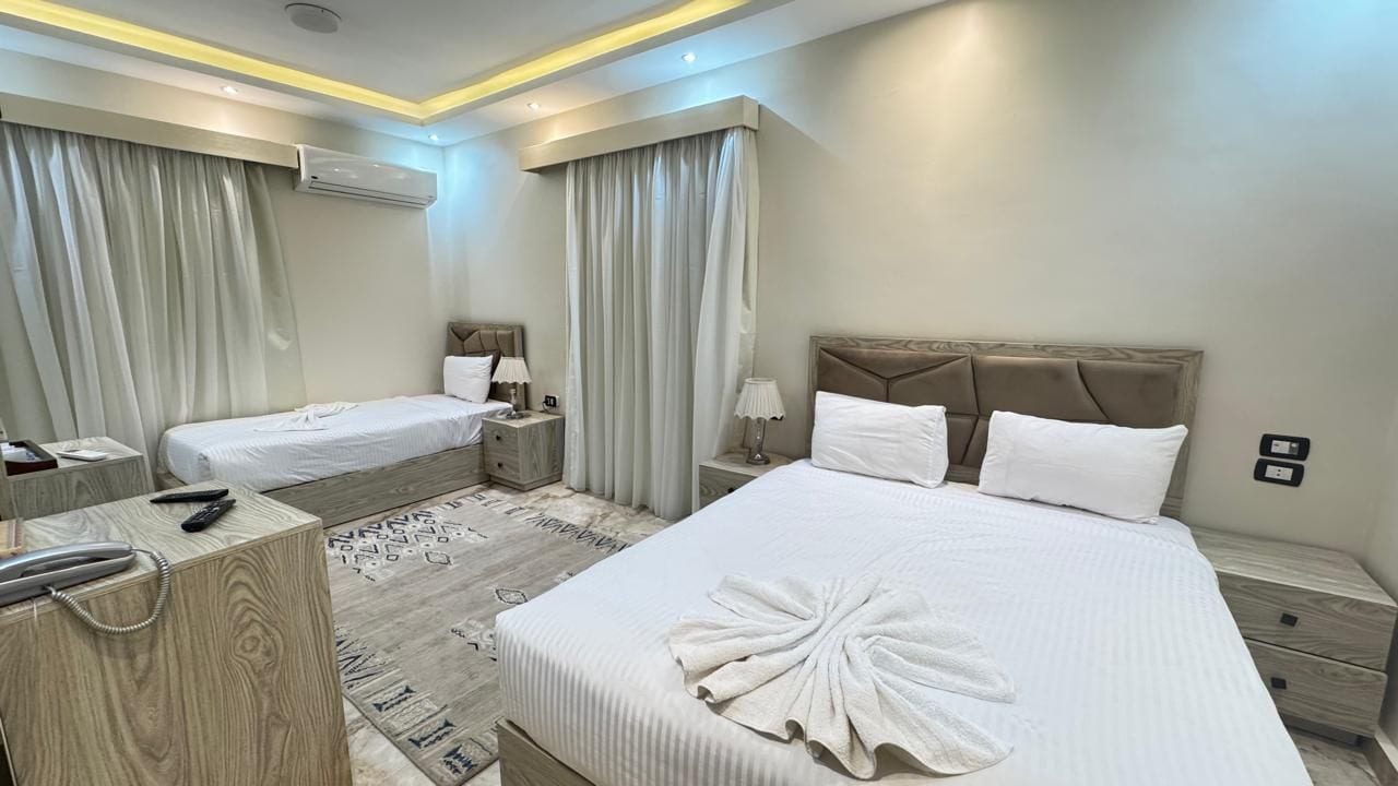 Une chambre d’hôtel avec deux lits, une table de chevet en bois et une autre table de chevet, ainsi qu’un climatiseur fixé au mur.