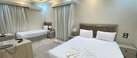Habitació d'hotel amb dos llits, una nitzeta de fusta, una tauleta de nit i un aire condicionat fixat a la paret.