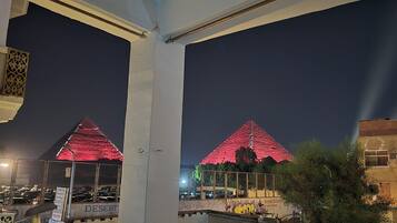 Vue de deux pyramides illuminées la nuit, avec un parking et un bâtiment couvert de graffitis au premier plan.