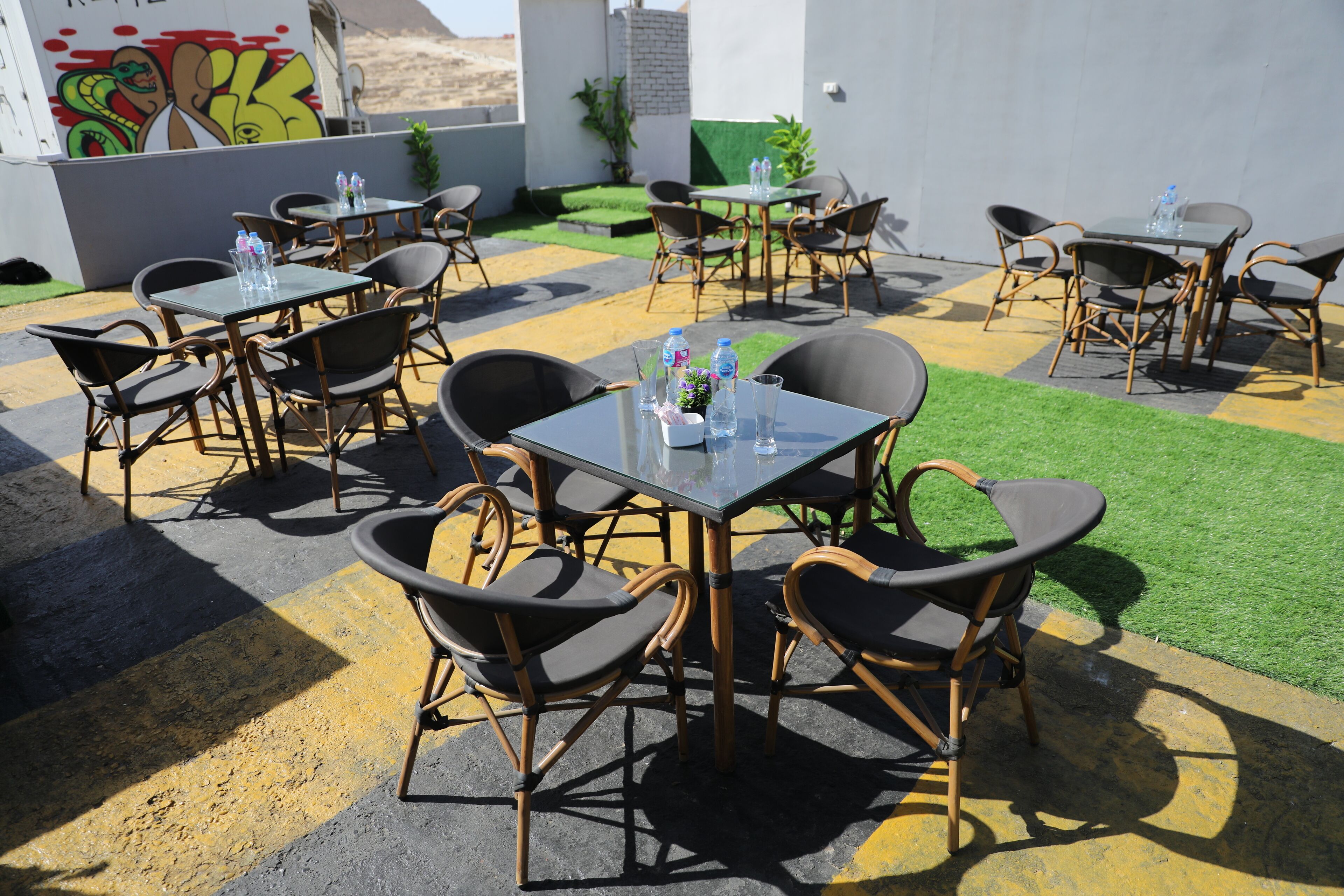 Un espace extérieur aménagé avec des tables et des chaises, dont certaines sont accompagnées de bouteilles d’eau et de verres.