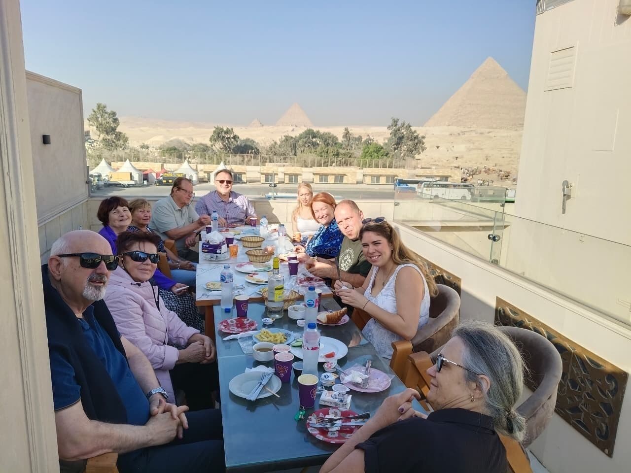 A group of people dining at a table with a view of the pyramids in the background.