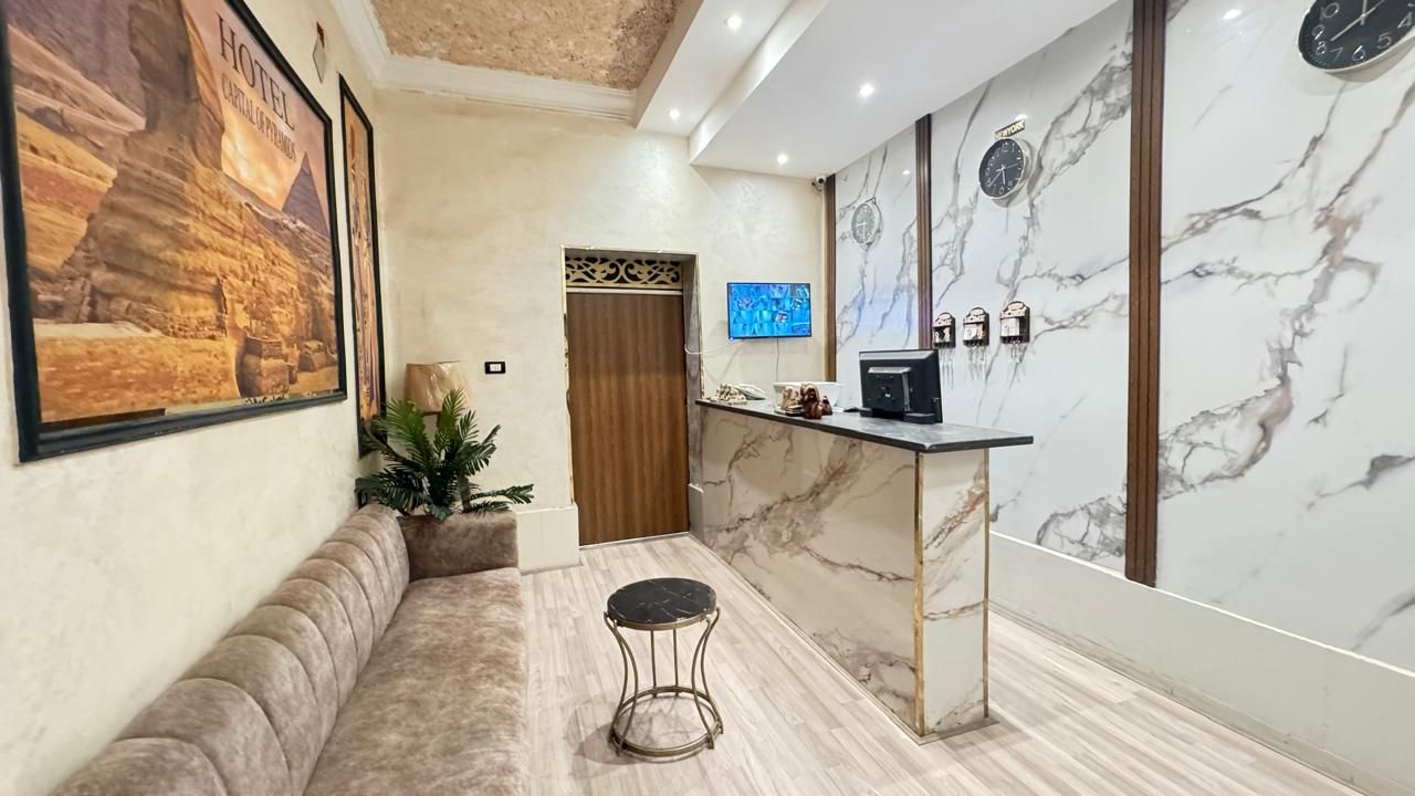 A hotel lobby with a reception desk, a sofa, a small round table, and a television screen.