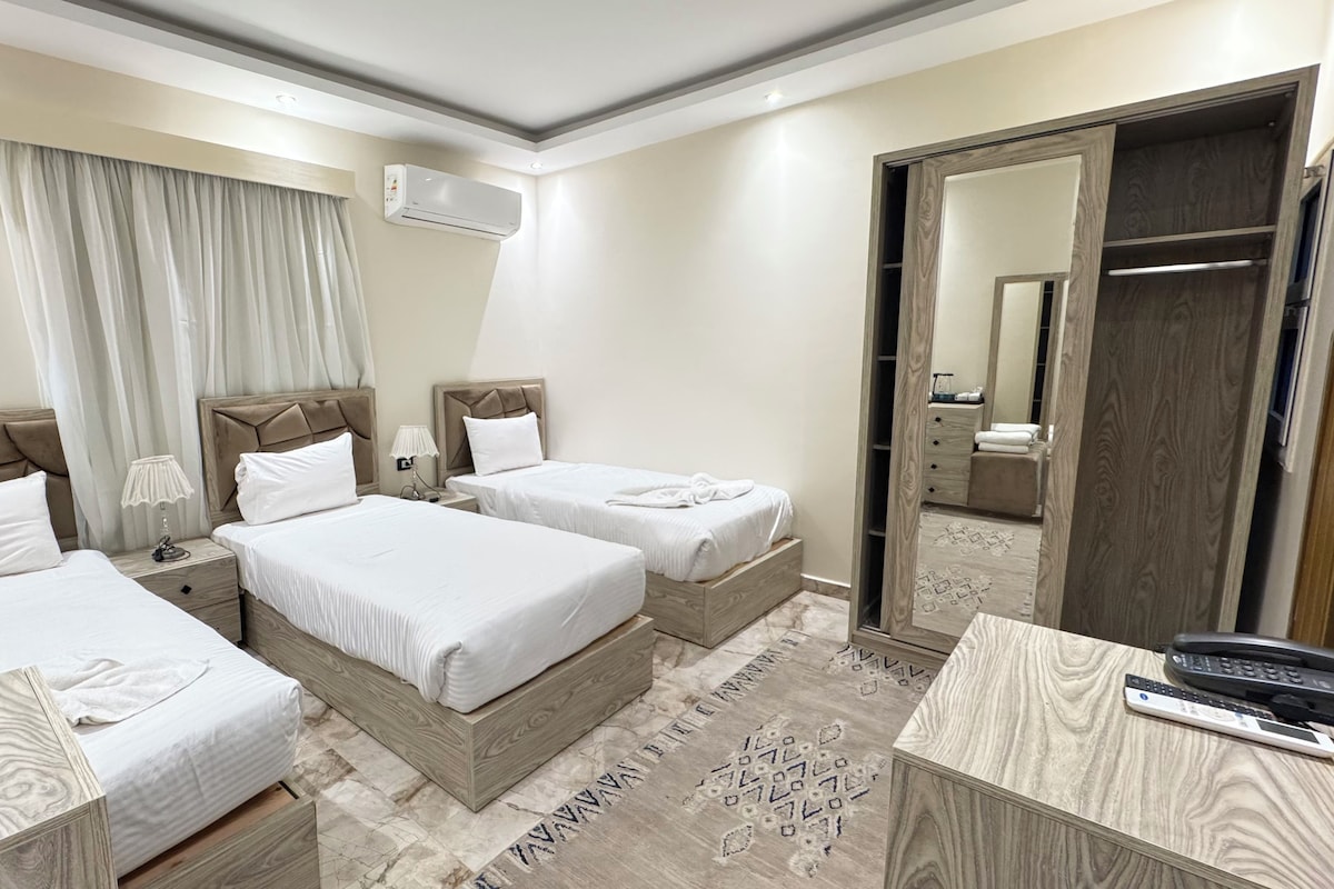 A hotel room with two beds, a wardrobe, a desk with a phone, and a mirror.