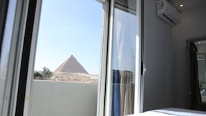 A hotel room with a large window offering a view of a pyramid. - Capital Of Pyramids Hotel (Giza)