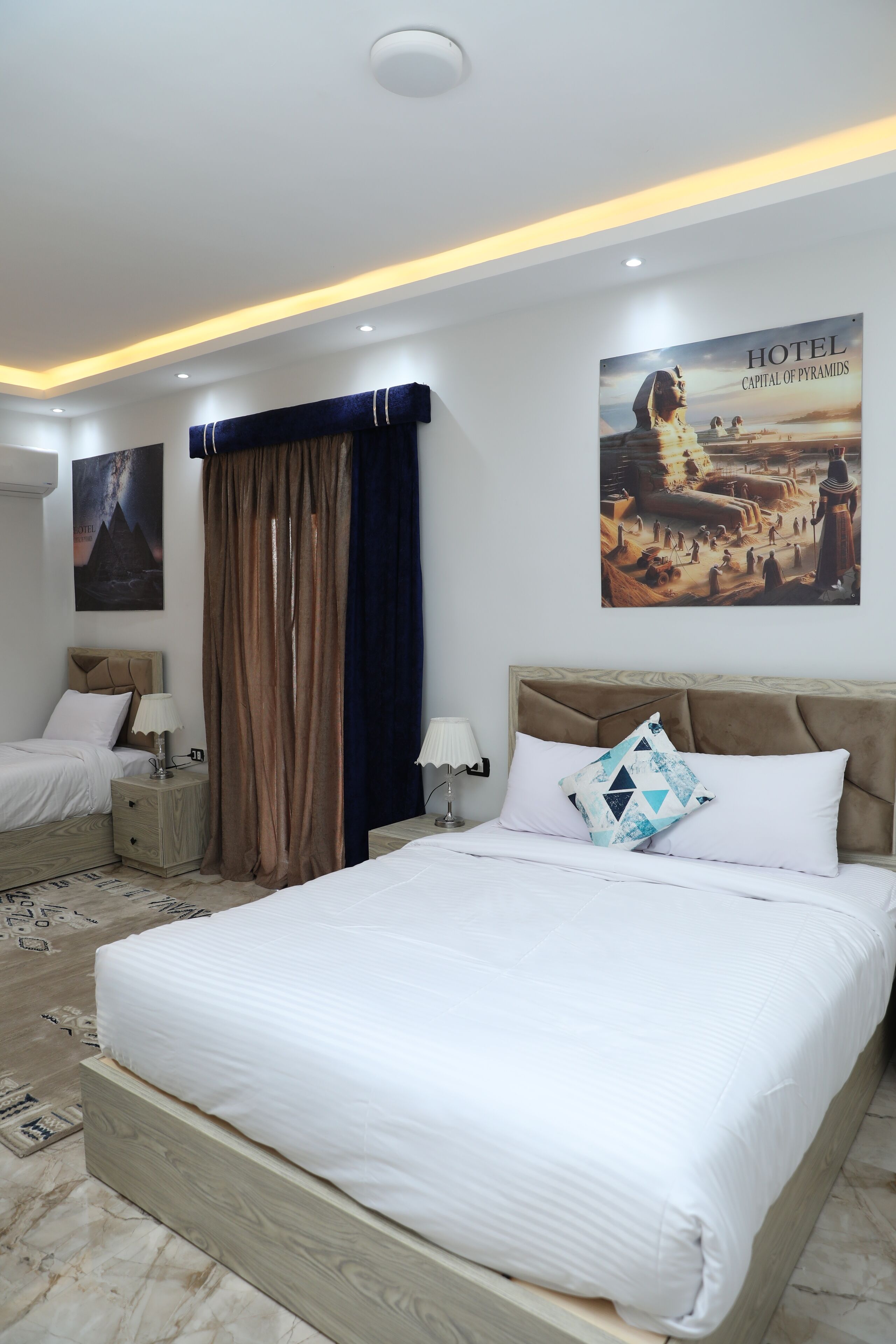 A modern hotel room with a large bed, a nightstand, a lamp, and a poster of the Sphinx.