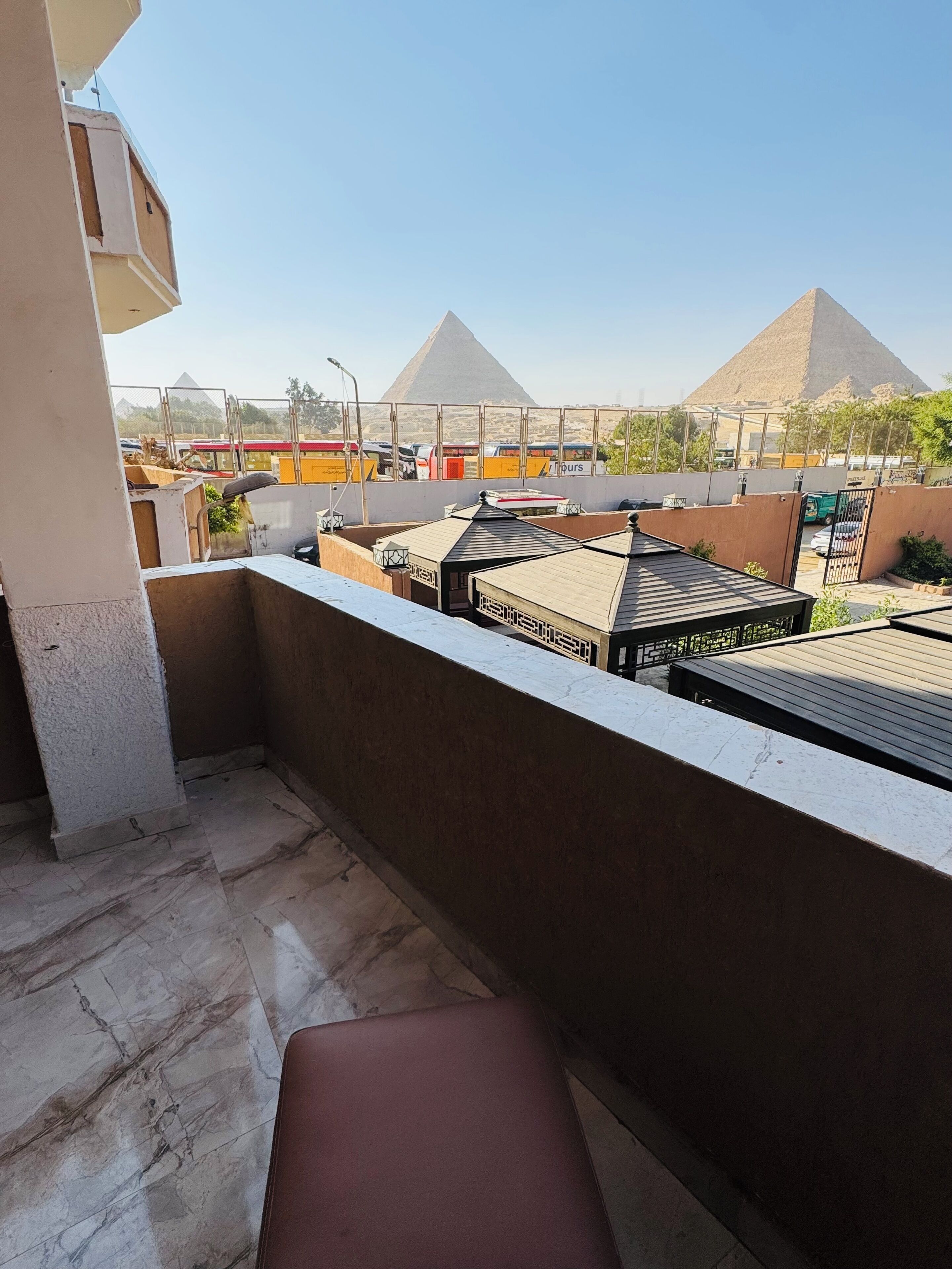 A balcony with a view of pyramids, a covered outdoor area, and a building with a beige facade.