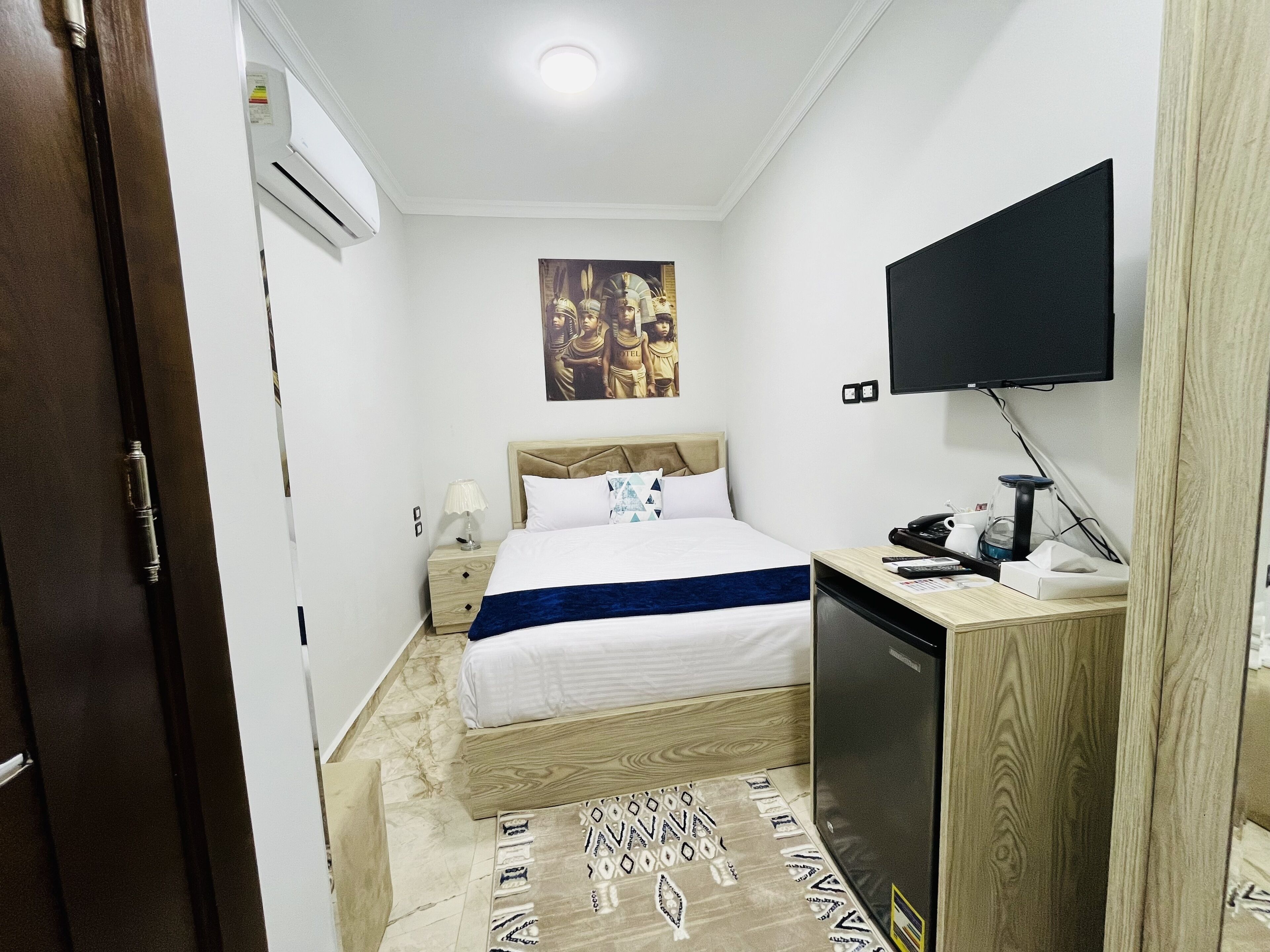A hotel room with a bed, a desk with a computer, a television, and a wall-mounted air conditioner.