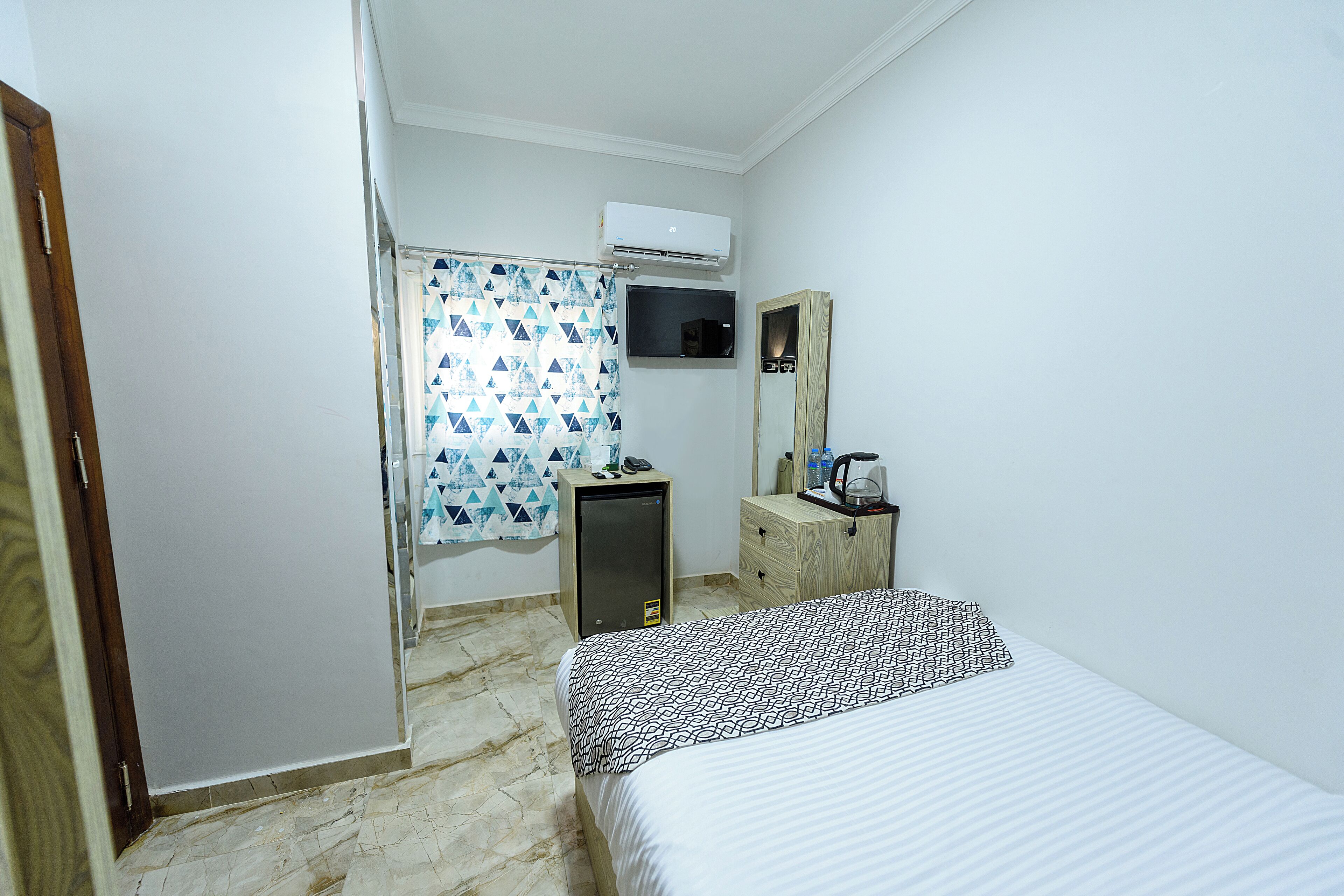 Una habitación pequeña y limpia con cama, escritorio, espejo y aire acondicionado.