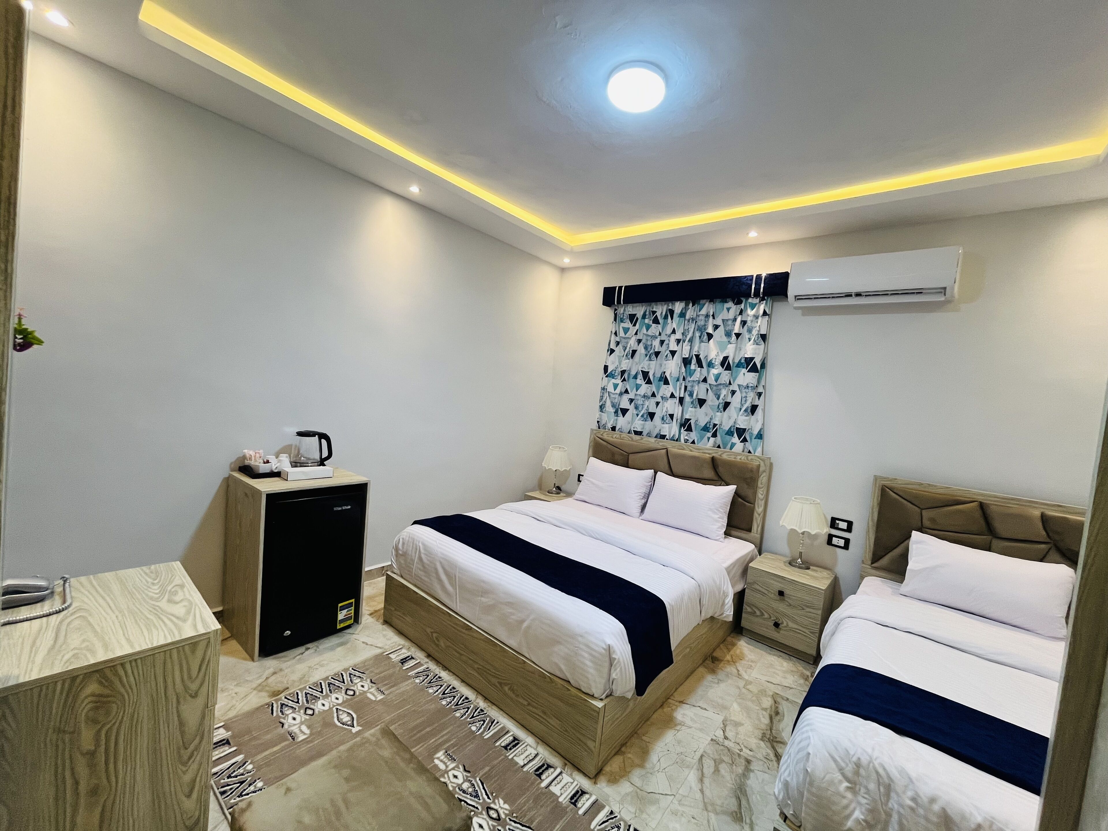 A modern hotel room with a bed, bedside tables, a desk, and an air conditioning unit.