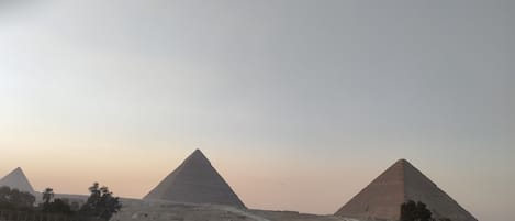 A view of three pyramids with a road and vehicles in the foreground.