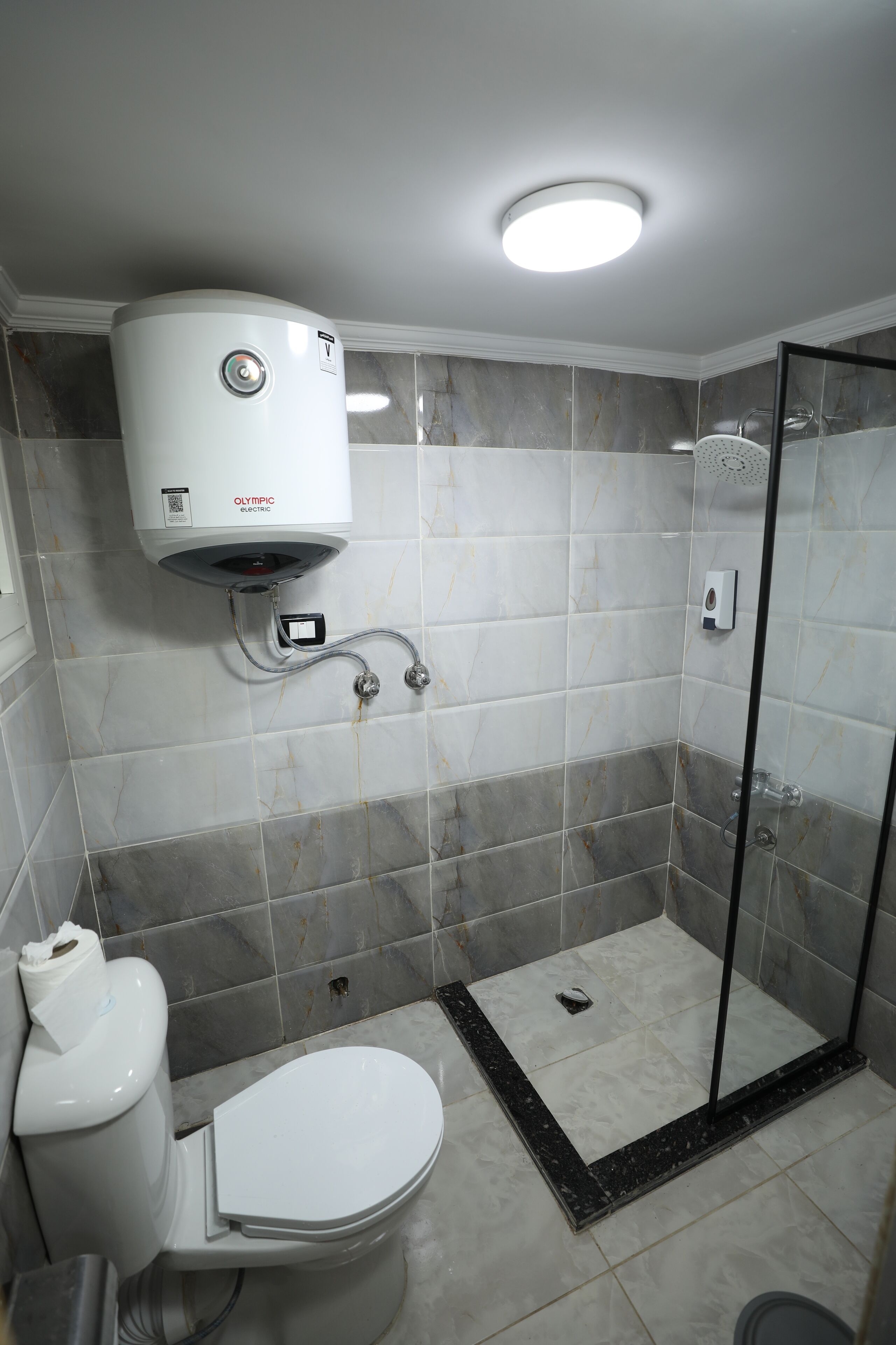 A bathroom with a toilet, a shower, and a built-in electric water heater.