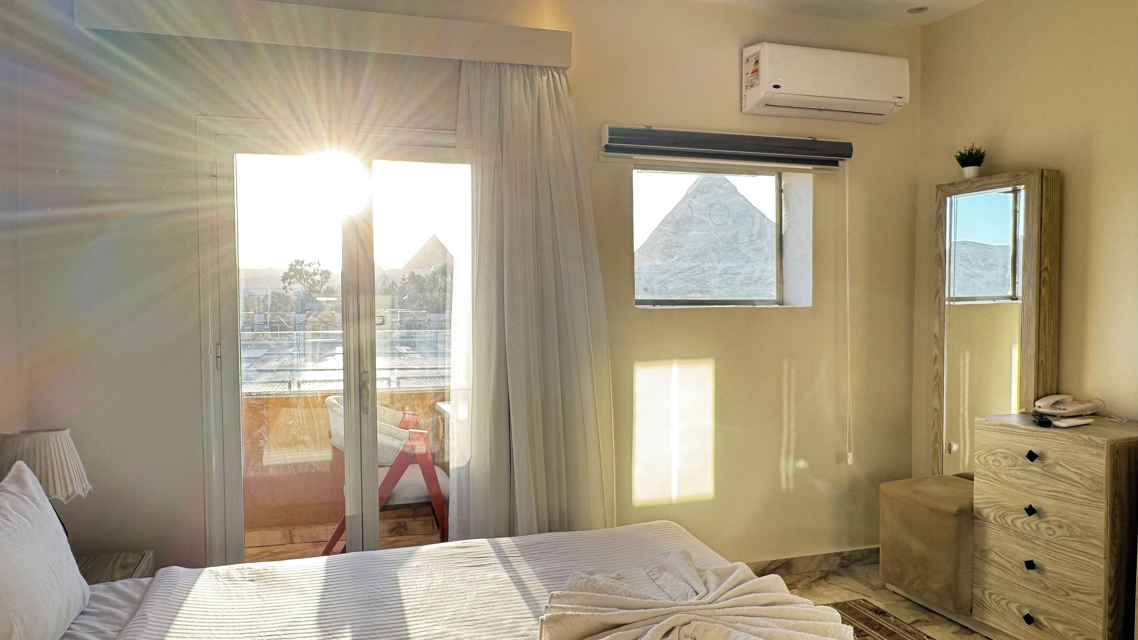 Una habitación de hotel con cama, cómoda, equipo de aire acondicionado, ventana con vista y puerta corredera.