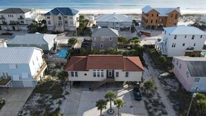 Un área residencial costera con varias casas, incluyendo una casa central con techo de tejas rojas, rodeada de edificios más pequeños y una playa al fondo.