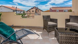 Ein Balkon mit Korbmöbeln, einem grünen Stuhl und einem Metallstuhl.