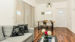 Ein Wohnzimmer mit grauem Sofa, einem Esstisch mit Stühlen und einer Vase mit Blumen auf einem Beistelltisch.