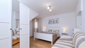 A bedroom with a bed, a bedside table with a lamp, a sofa, and a painting on the wall.