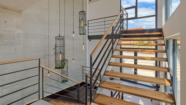 A modern staircase with wooden steps and metal railings, leading to a balcony with large windows.