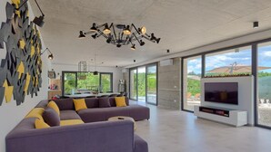 A modern living room with a sectional sofa, a TV, and a dining area with a view of greenery.