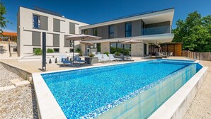 A modern two-story house with a swimming pool, outdoor seating, and a covered patio area.