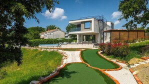 A modern two-story house with a swimming pool, a tennis court, and a landscaped garden.