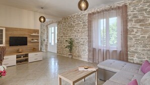 A spacious living area with a stone wall, a television, a wooden coffee table, and a sofa. - Cozy apartment in Umag with private swimming pool, can be inside or outside (Umag)