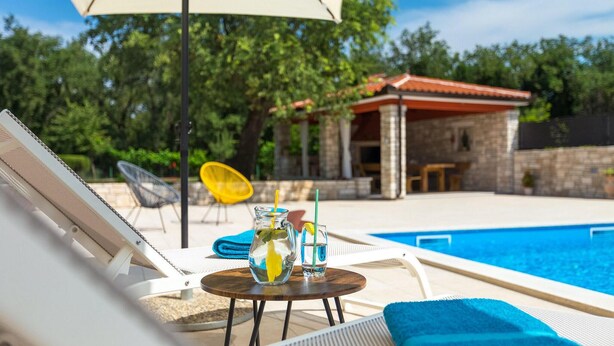 A poolside area with lounge chairs, a table with drinks, and a building in the background. - Cozy apartment in Umag with private swimming pool, can be inside or outside (Umag)