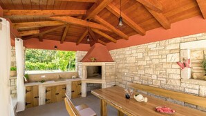An outdoor kitchen with stone walls, wooden beams, and a dining table with a bench. - Cozy apartment in Umag with private swimming pool, can be inside or outside (Umag)