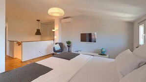 Une chambre à coucher moderne avec un grand lit, un téléviseur fixé au mur, un bureau avec un globe terrestre et une plante en pot.