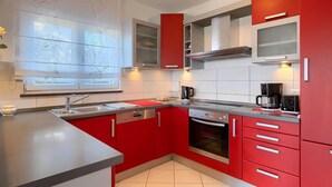 Une cuisine moderne avec des meubles de couleur rouge, un évier en acier inoxydable et un four encastré.