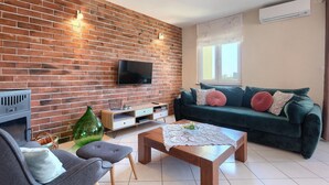 Un salon avec un mur en briques, un téléviseur à écran plat, un canapé vert, une table basse et une cheminée.