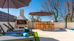 Une terrasse extérieure équipée d’un barbecue, de chaises longues, d’une table avec des chaises et d’une piscine.