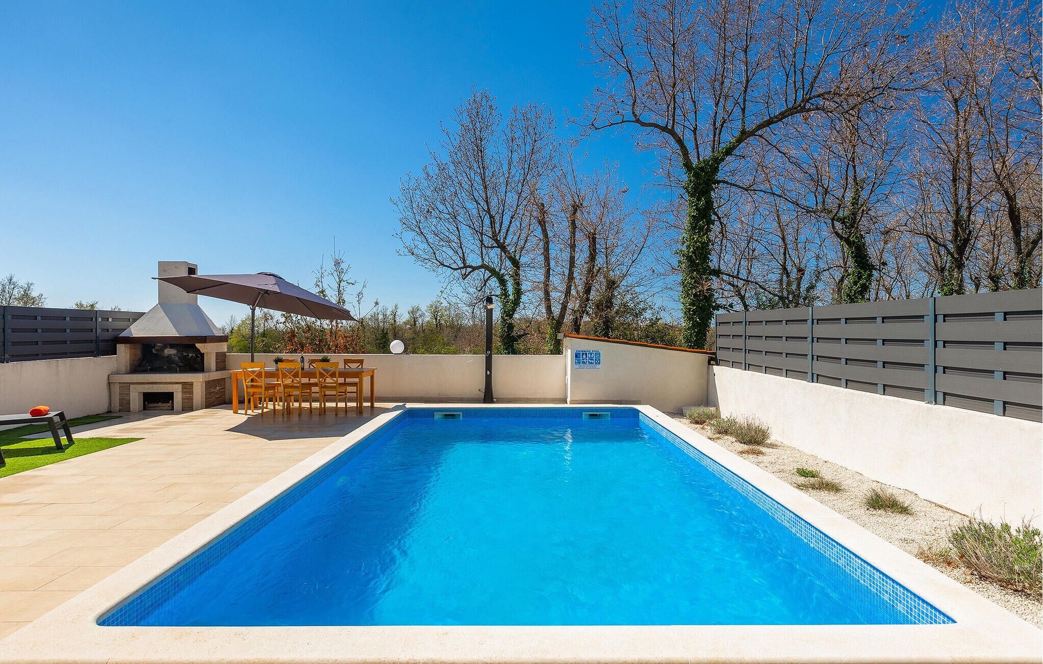 Une piscine rectangulaire dont le bord est recouvert de carreaux, entourée d’une terrasse de couleur claire.