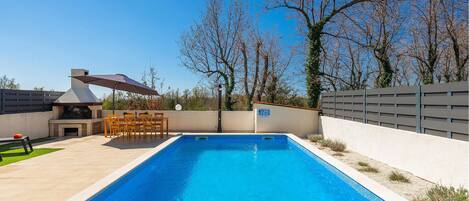 Une piscine rectangulaire dont le bord est recouvert de carreaux, entourée d’une terrasse de couleur claire.