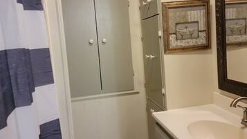 Une salle de bain avec un rideau de douche, un lavabo, un miroir et un meuble de rangement.