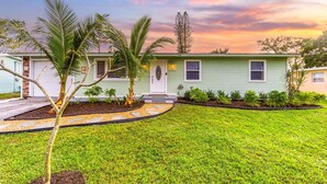 A single-story house with a green exterior, a front porch, and a well-maintained lawn. - Arcade · Firepit · 2 King Beds + Workspace (Stuart)