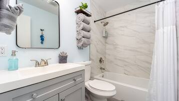 A modern bathroom with a white sink, a toilet, a bathtub, and a shower curtain.