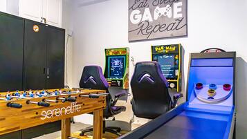 Una habitación con una mesa de fútbol de mesa, dos sillas de juego, dos juegos de arcade y un letrero en la pared.