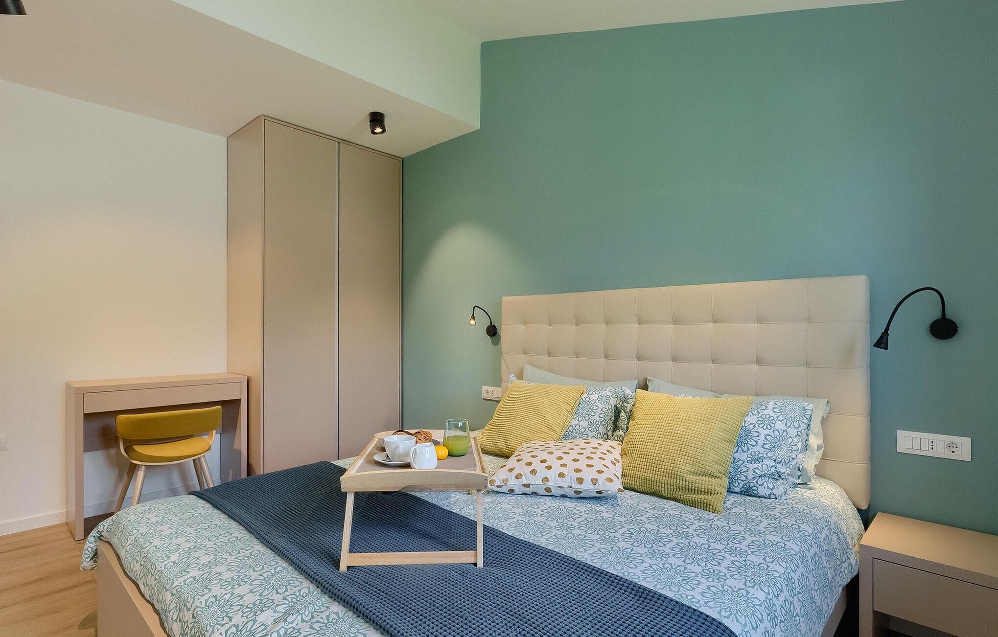 A bedroom with a bed, bedside table, lamp, and a chair.