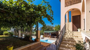 Un edificio con piscina, escaleras exteriores y un jardín con plantas en macetas.