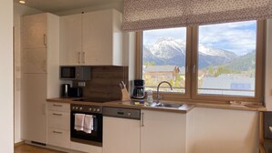 Una cucina moderna con forno integrato, microonde e macchina del caffè, un'ampia finestra con vista sulle montagne e pavimento in legno.