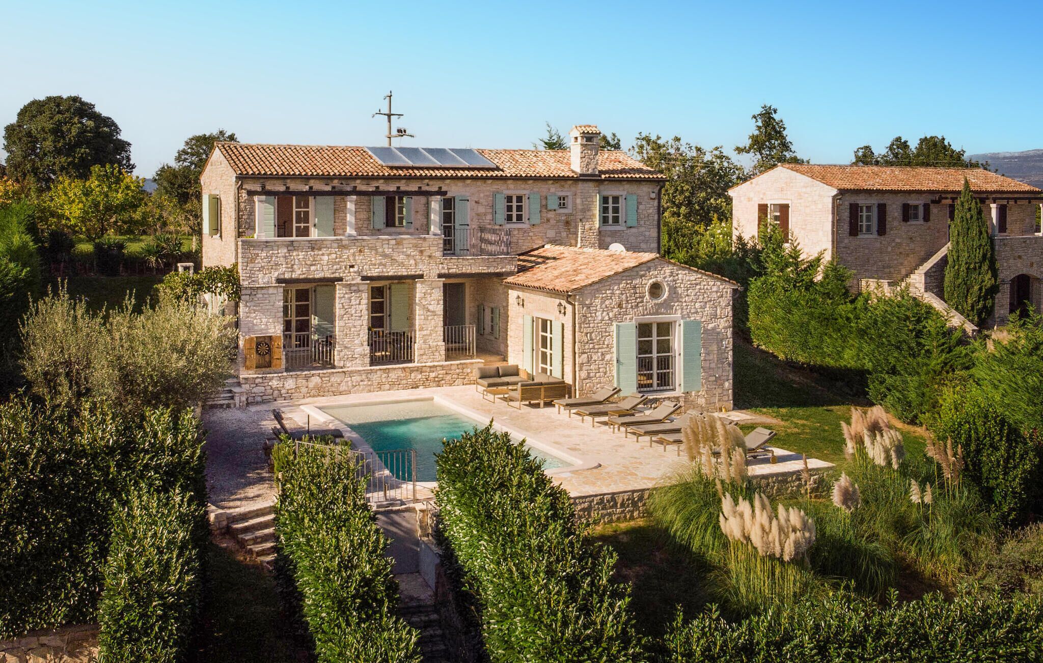 Una villa de piedra con piscina, rodeada de exuberante vegetación y un paisaje montañoso.