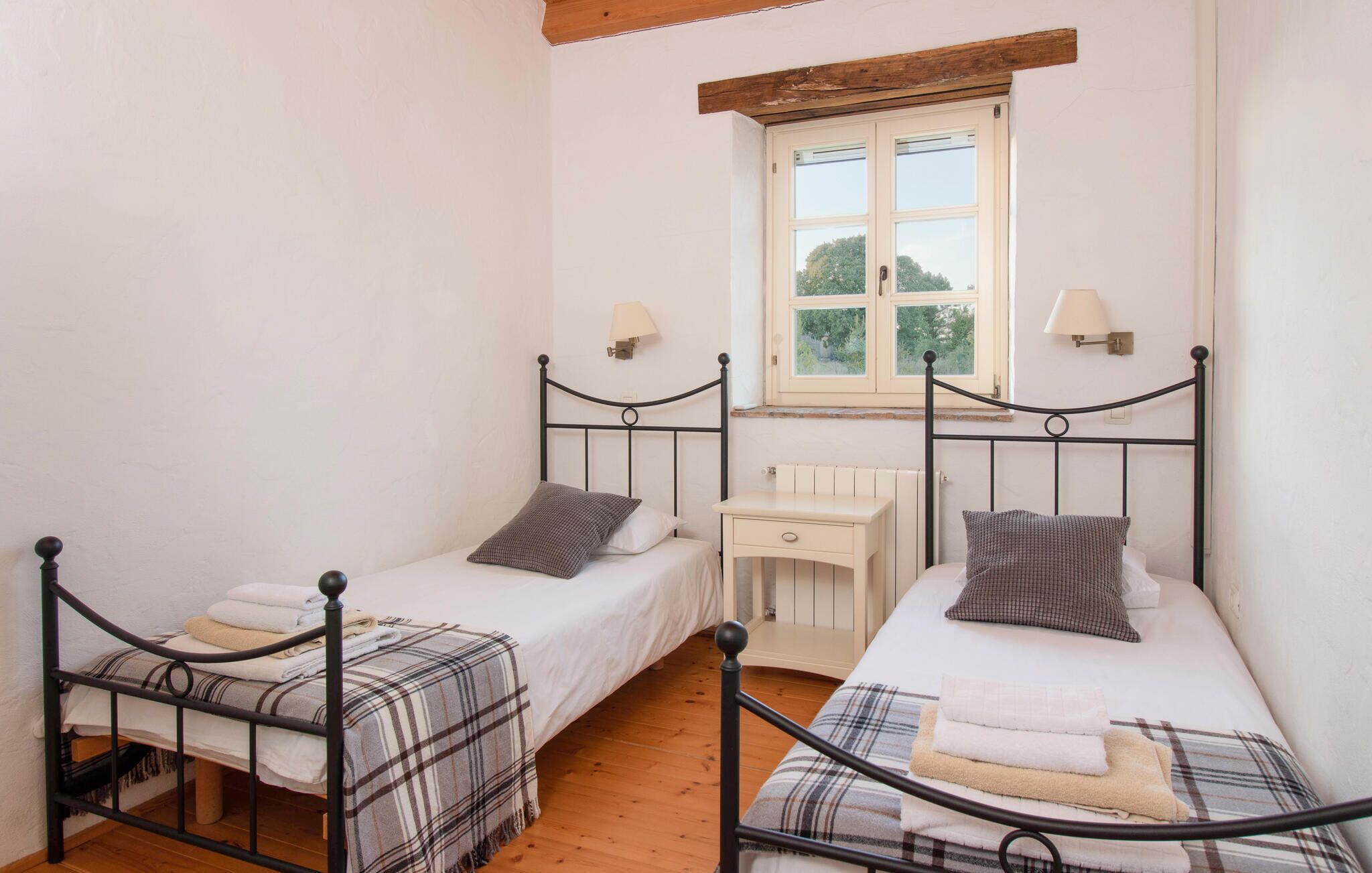 Un dormitorio con dos camas individuales, un escritorio pequeño y una ventana con vistas a la vegetación.