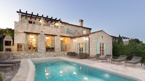 Une maison en pierre avec une piscine, un espace salon extérieur et une pergola.