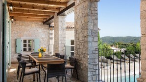 Une terrasse en pierre avec une table et des chaises en bois, un mur en pierre et une vue sur un paysage montagneux.