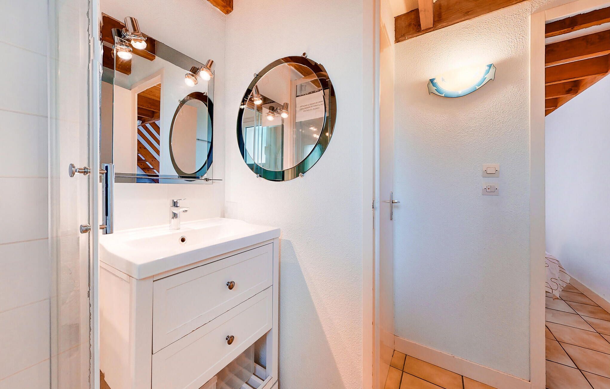 A bathroom with a white vanity, two round mirrors, and a light fixture above the mirror.