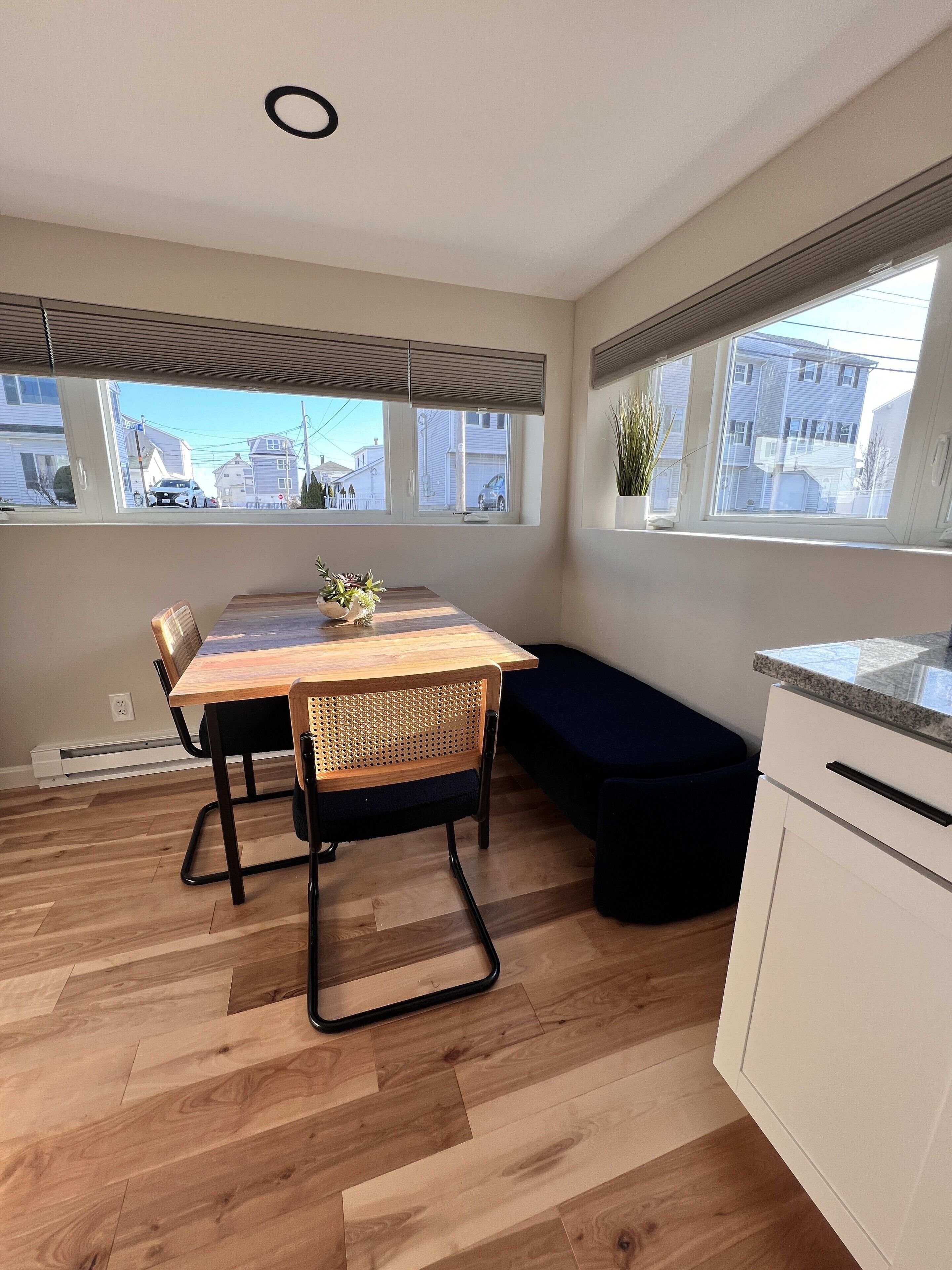 Een moderne keuken met een houten eettafel, een bank en grote ramen met uitzicht op de straat.